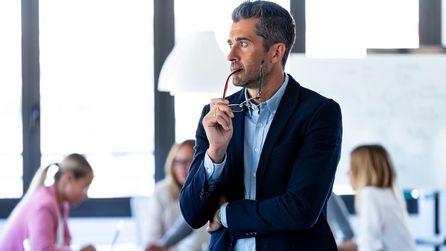 Shot of handsome businessman looking to sideways while his colleagues are working on coworking place.