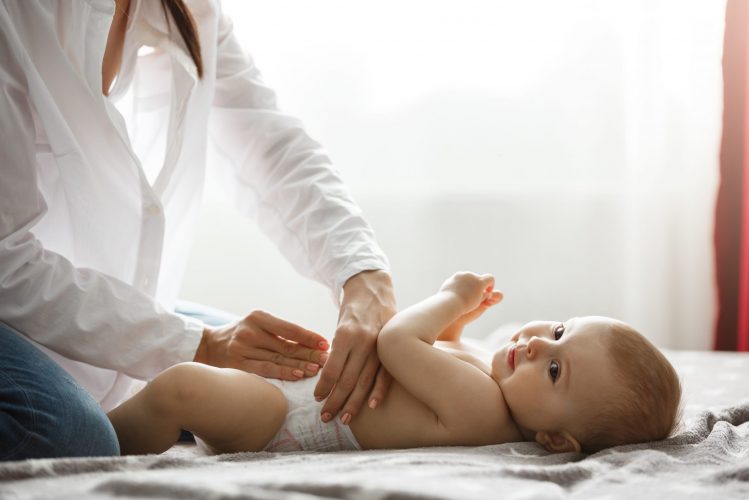 Young mom gentle putting diaper on one years old little son with her tender hands before going out for a walk in park with her husband. Spending special time with family. Family concept.