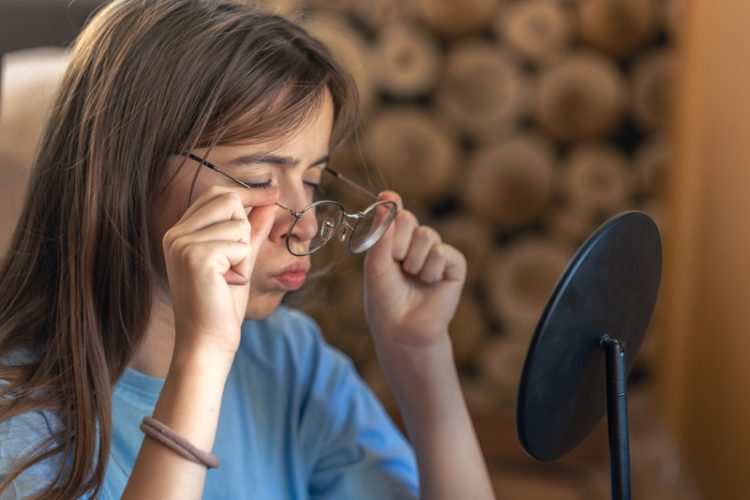 A beautiful girl in glasses looks at herself in the mirror. Morning routine. High quality photo. The girl looks at herself in the mirror at home.
