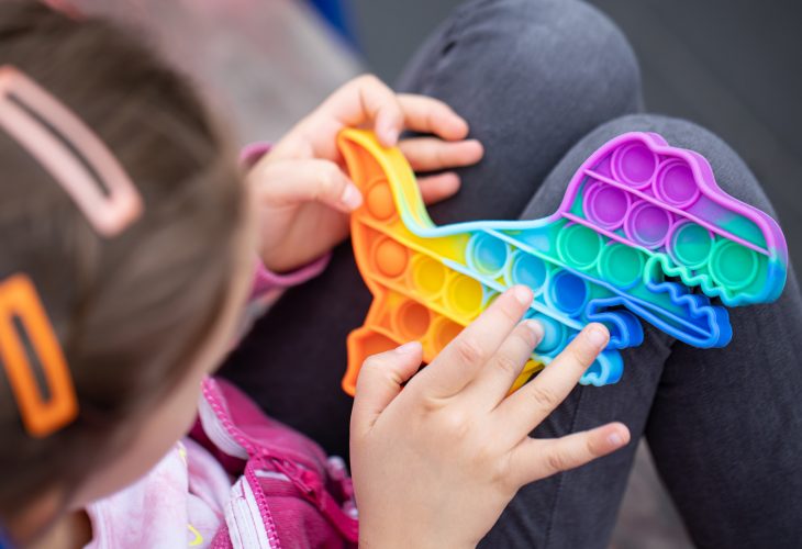 Popular colorful anti-stress touch toy dragon shaped fidgets push pop it in the hands of a child.