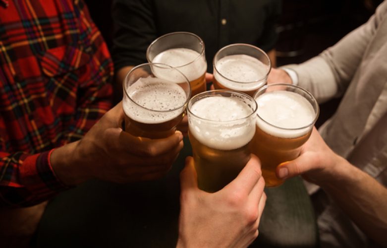 Close-up of five men toasting with beer while sitting in beer pub together