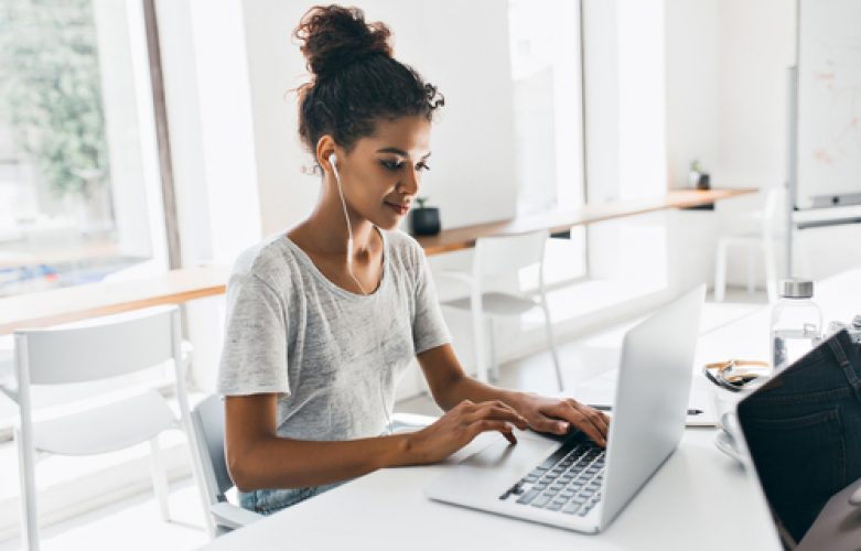 Romantic african girl with trendy hairstyle sitting at her workplace and analysing data. Indoor portrait of black female student working with laptop before exam.