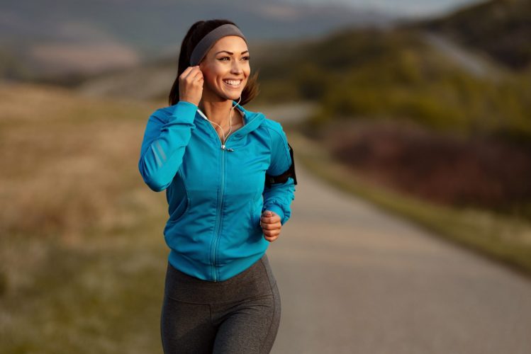 Happy athletic woman listening music on earphones while running in nature in the morning. Copy space.