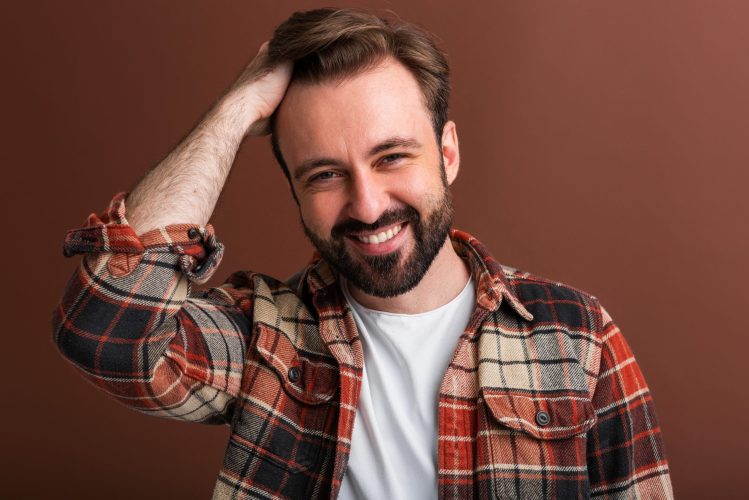 portrait of sexy goodlooking attractive stylish bearded man on brown background isolated in vintage checkered shirt smiling happy with cool hairstyle