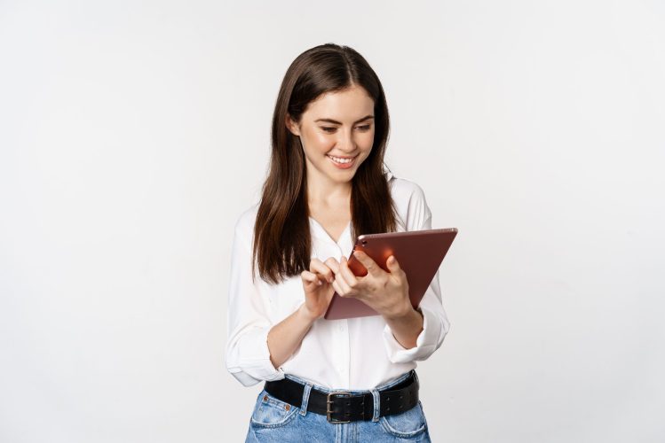 Portrait of smiling corporate woman looking at digital tablet, working, standing over white background Portrait of smiling corporate woman looking at digital tablet, working, standing over white background.